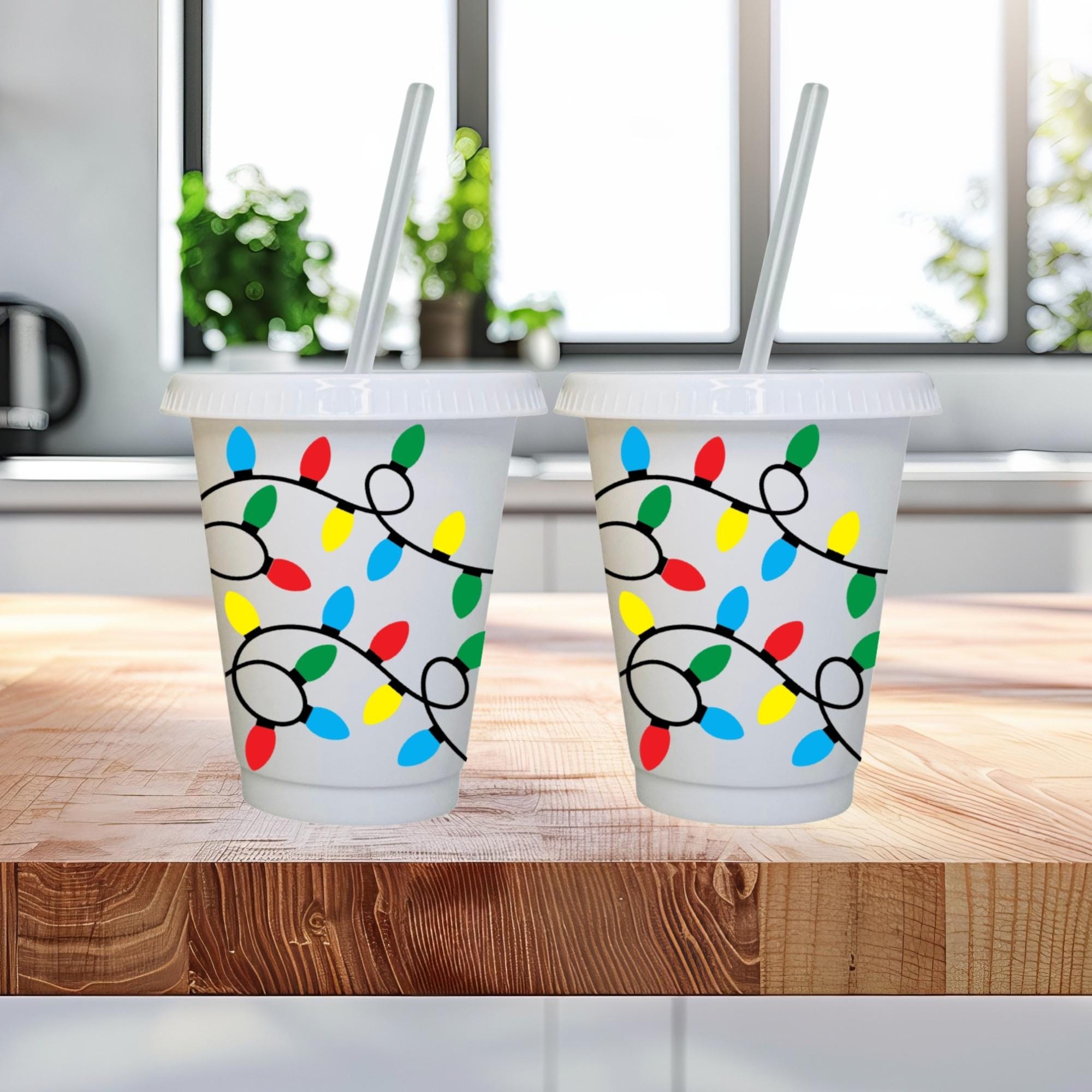 Two white cold cups with lids and straws with Christmas light design on them.