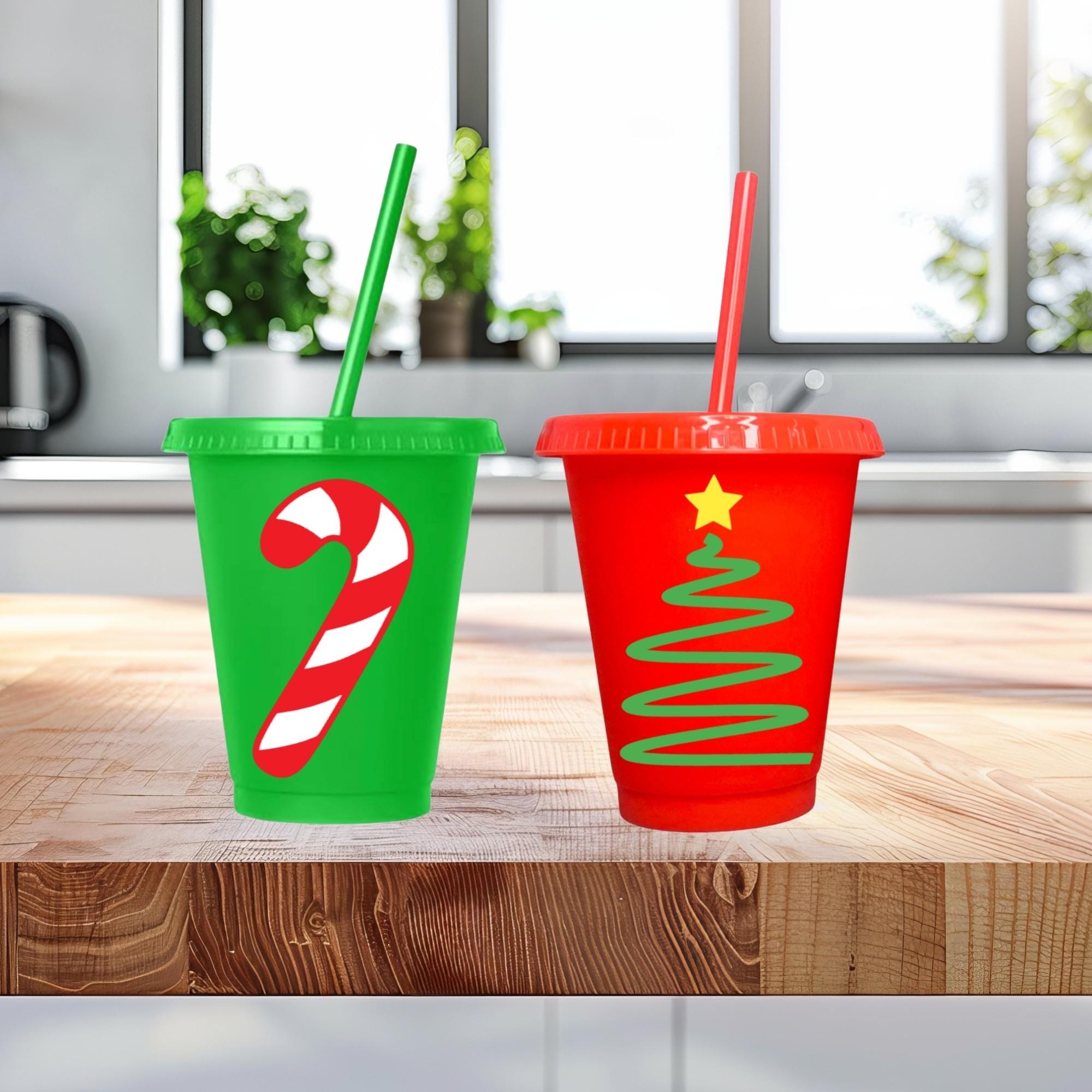 Two Christmas-themed cups with candy cane and tree designs on a wooden surface.