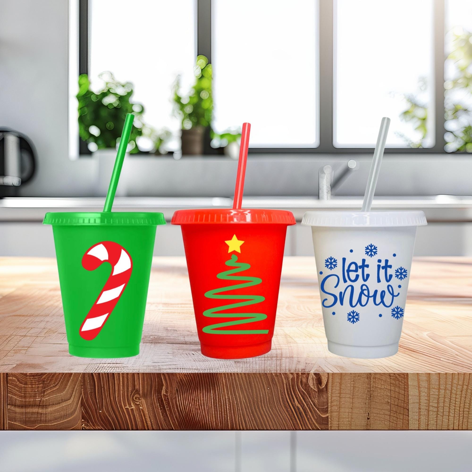 Three Christmas-themed cups with straws on a wooden surface.