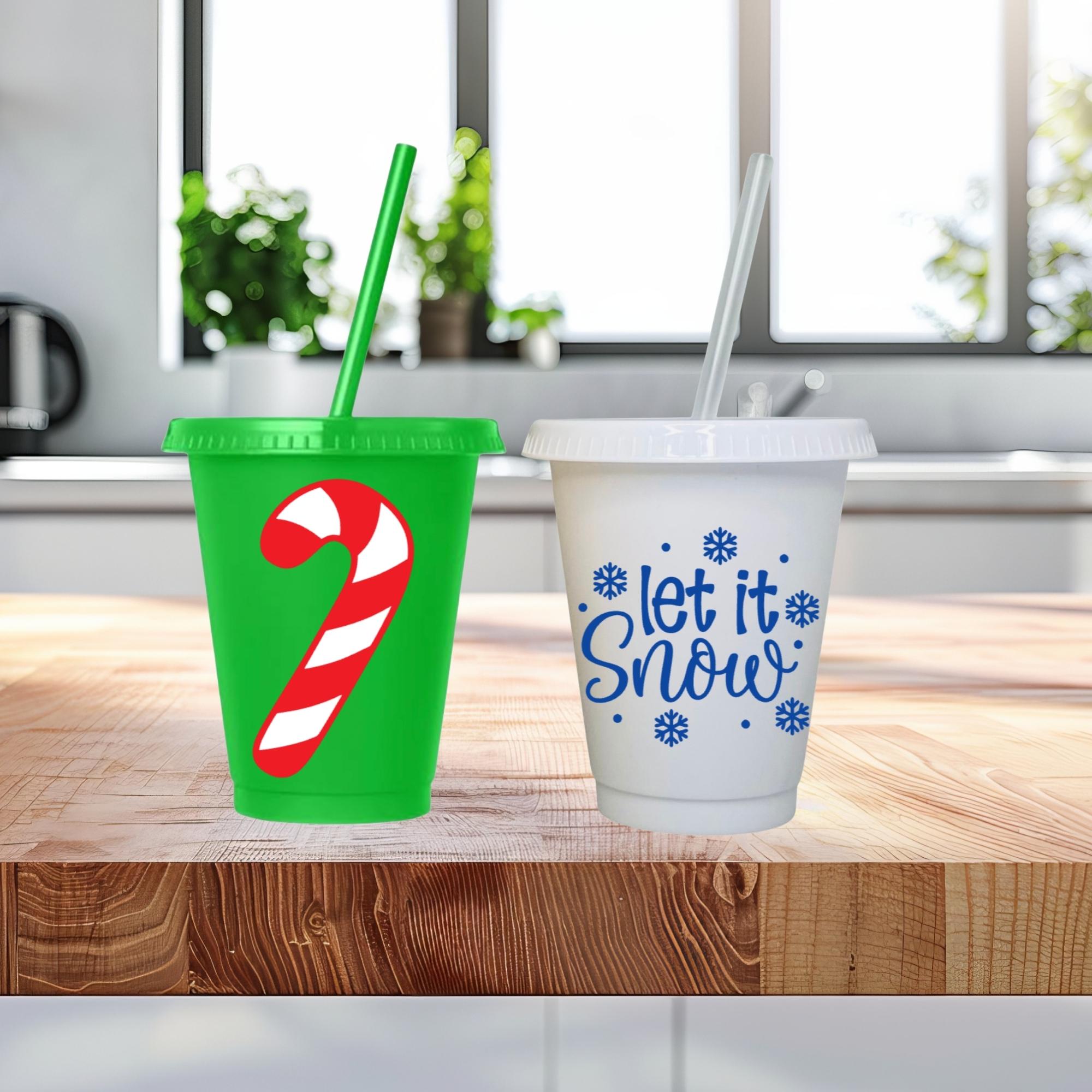 Two Christmas-themed cups with a green one featuring a candy cane design and a white one with 'let it snow' text, on a wooden surface.