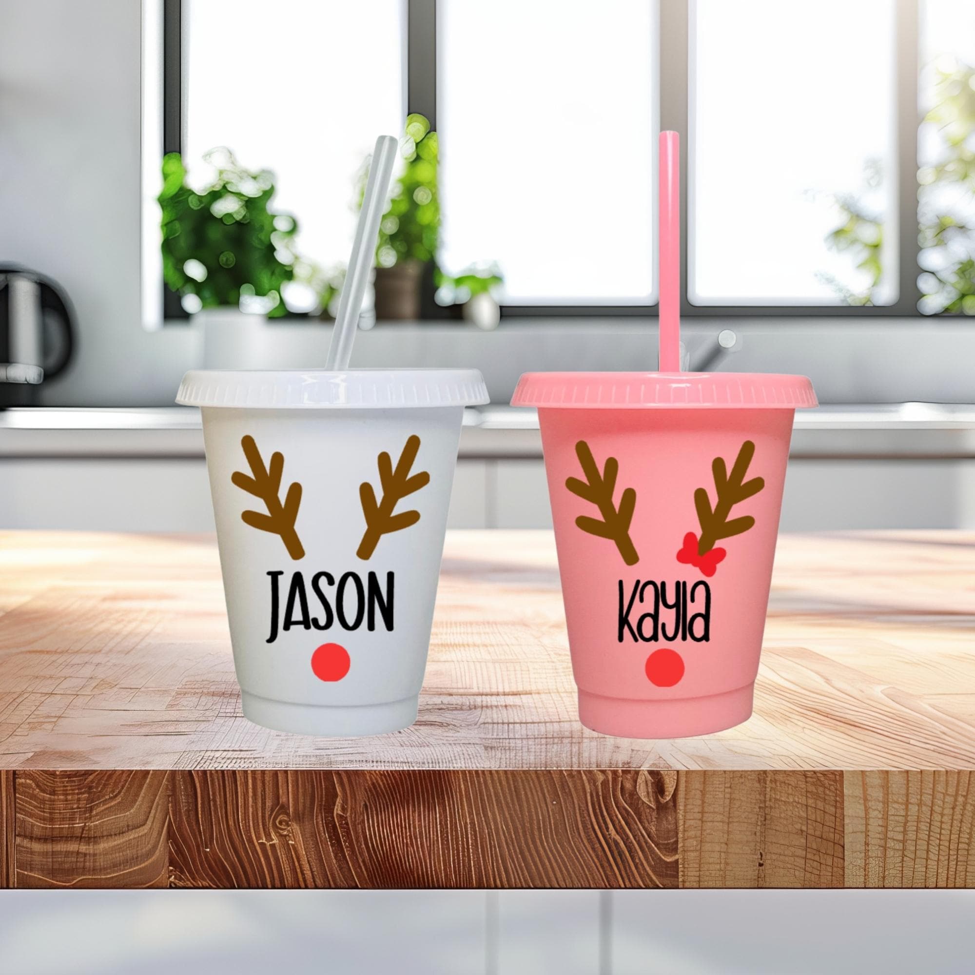 Two personalized tumblers with reindeer antlers and names on a wooden surface.