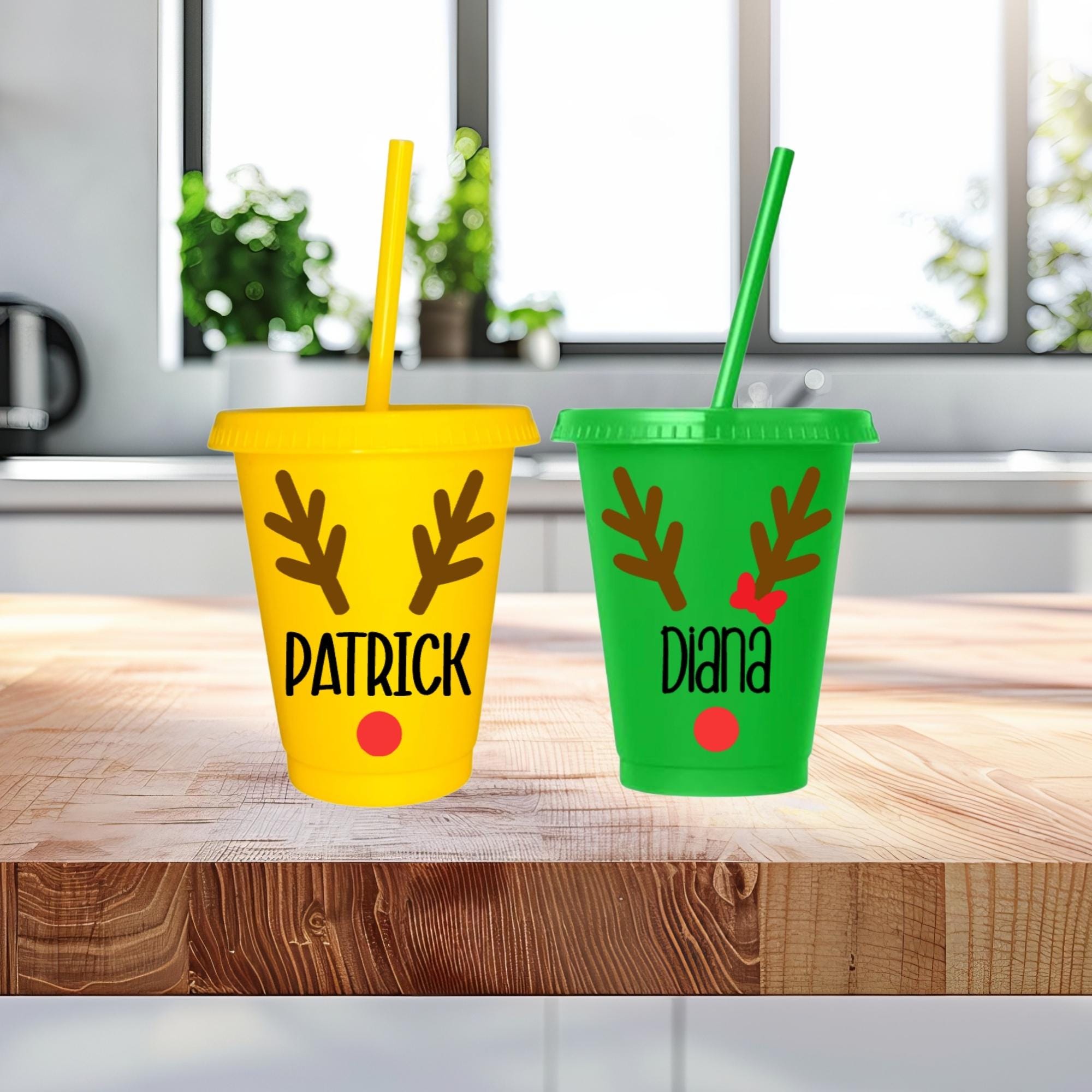 Two colorful tumblers with reindeer antlers and names on a wooden surface.
