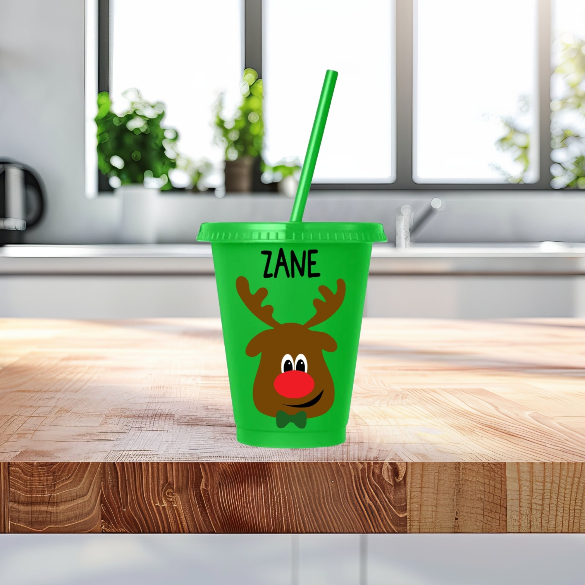 Green tumbler with reindeer design and straw on a wooden surface