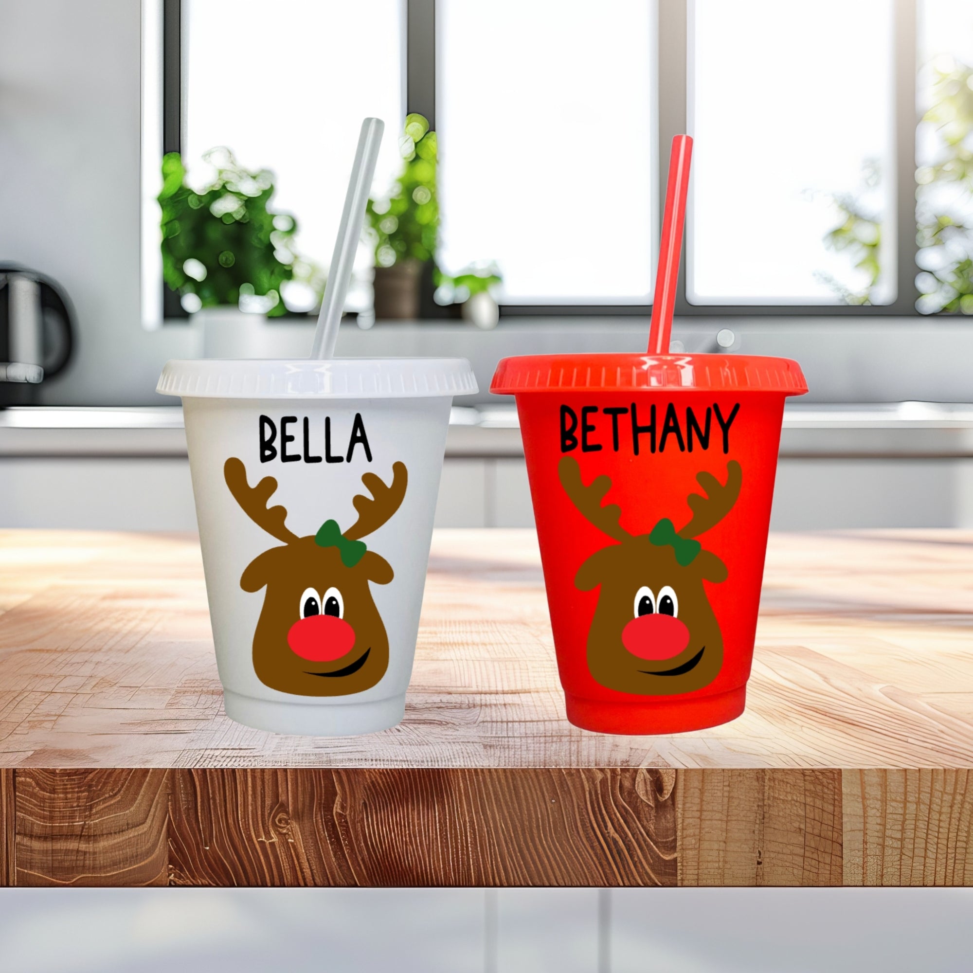 Two reindeer-themed cups with names 'Bella' and 'Bethany' on a wooden surface.